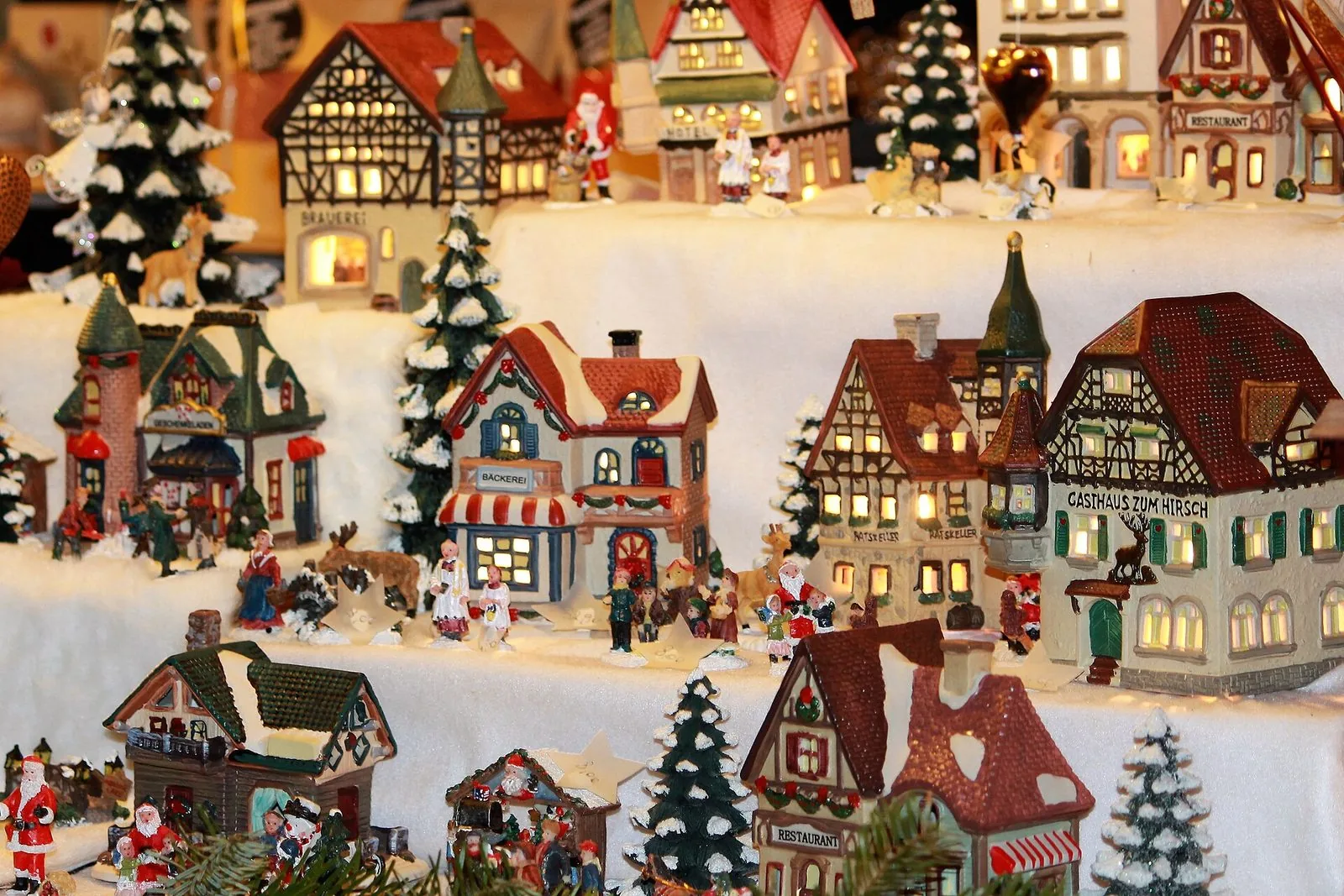 Un banco del Mercatino di Natale di Bolzano con un villaggio natalizio in miniatura: casette in ceramica illuminate dall'interno, alberelli innevati, statuine e piccoli Babbo Natale disposti su gradini coperti di ovatta bianca