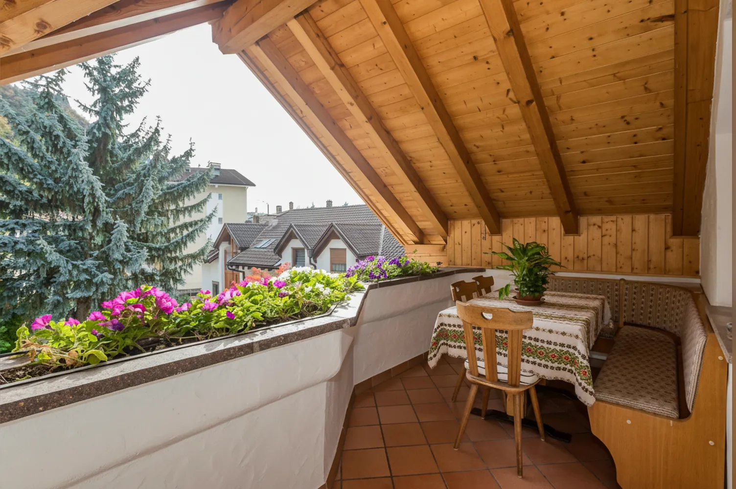 La terrazza coperta con il tavolo, la panca, i fiori sulla balaustra e la vista sugli alberi